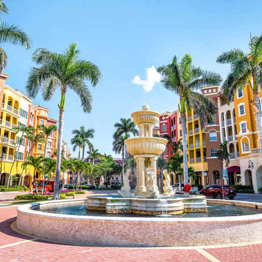 Naples, USA - April 30, 2018: Bayfront condos, condominiums colorful, multicolored, multi-colored buildings with fountain, water, palm trees, blue sky in residential community